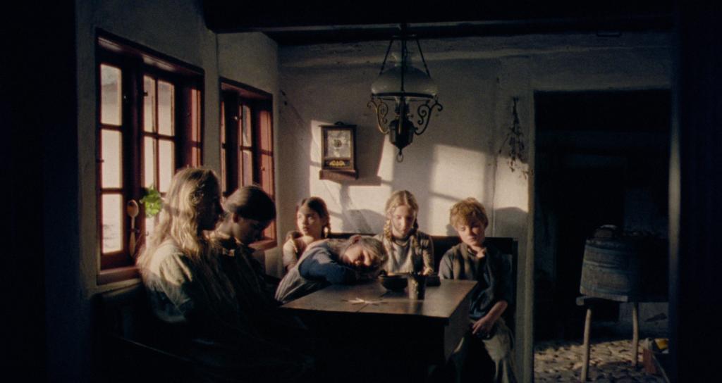 La jeune protagoniste et ses jeunes frères et soeurs, l'air soucieux, autour d'une table dans une pièce sombre, à côté d'une fenêtre laissant passer des rayons de lumière, qui illuminent leurs visages