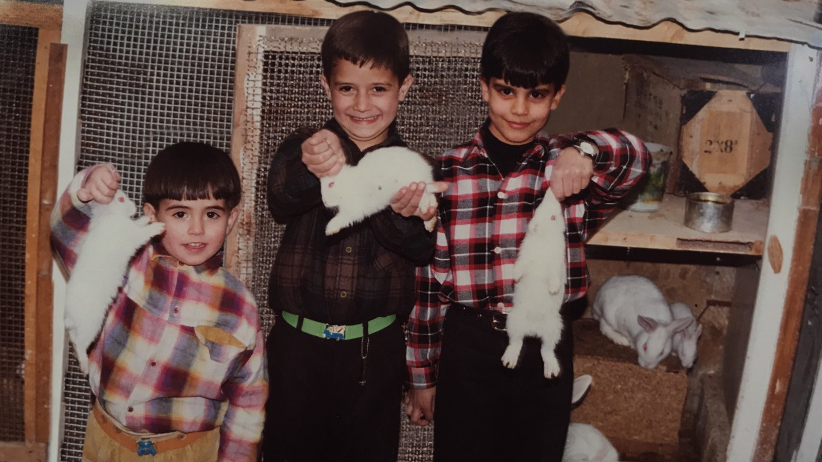 Photo d'archive : fratrie de trois enfants qui tiennent chacun un lapin dans leurs mains. Ils sourient en regardant l'objectif.