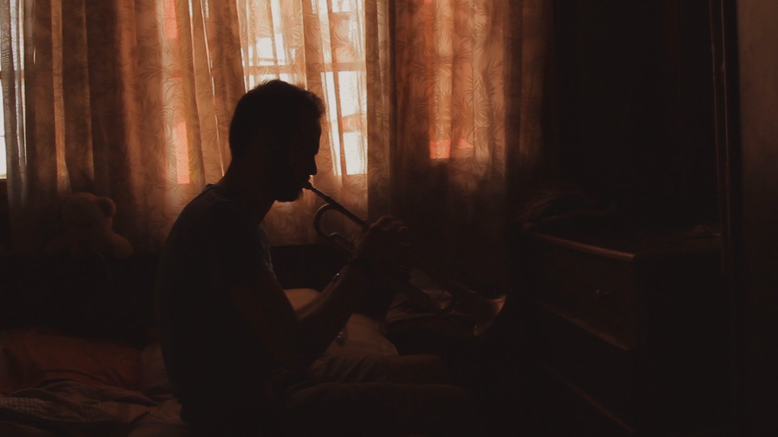 Silhouette d'un homme de profil jouant de la trompette dans la pénombre.