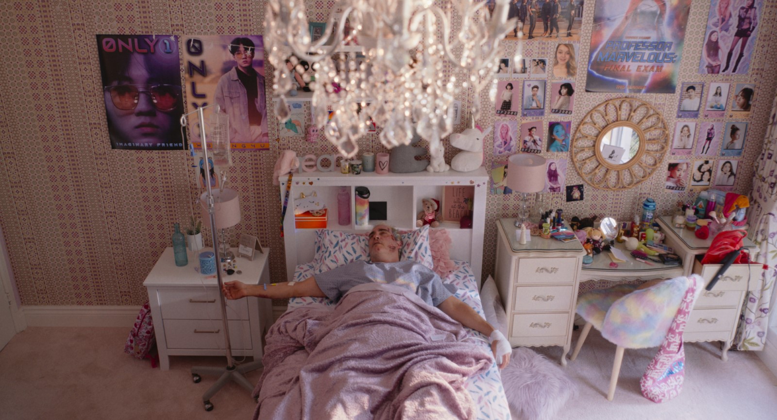Beau couché en tenue d'hôpital et branché à une perfusion dans le lit d'une chambre adolescente tout en rose avec des posters de k-pop